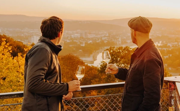 Zwei Männer von der Seite halten Weingläser und blicken auf die Stadt Koblenz beim Sonnenuntergang ©Koblenz-Touristik GmbH, Philip Bruederle